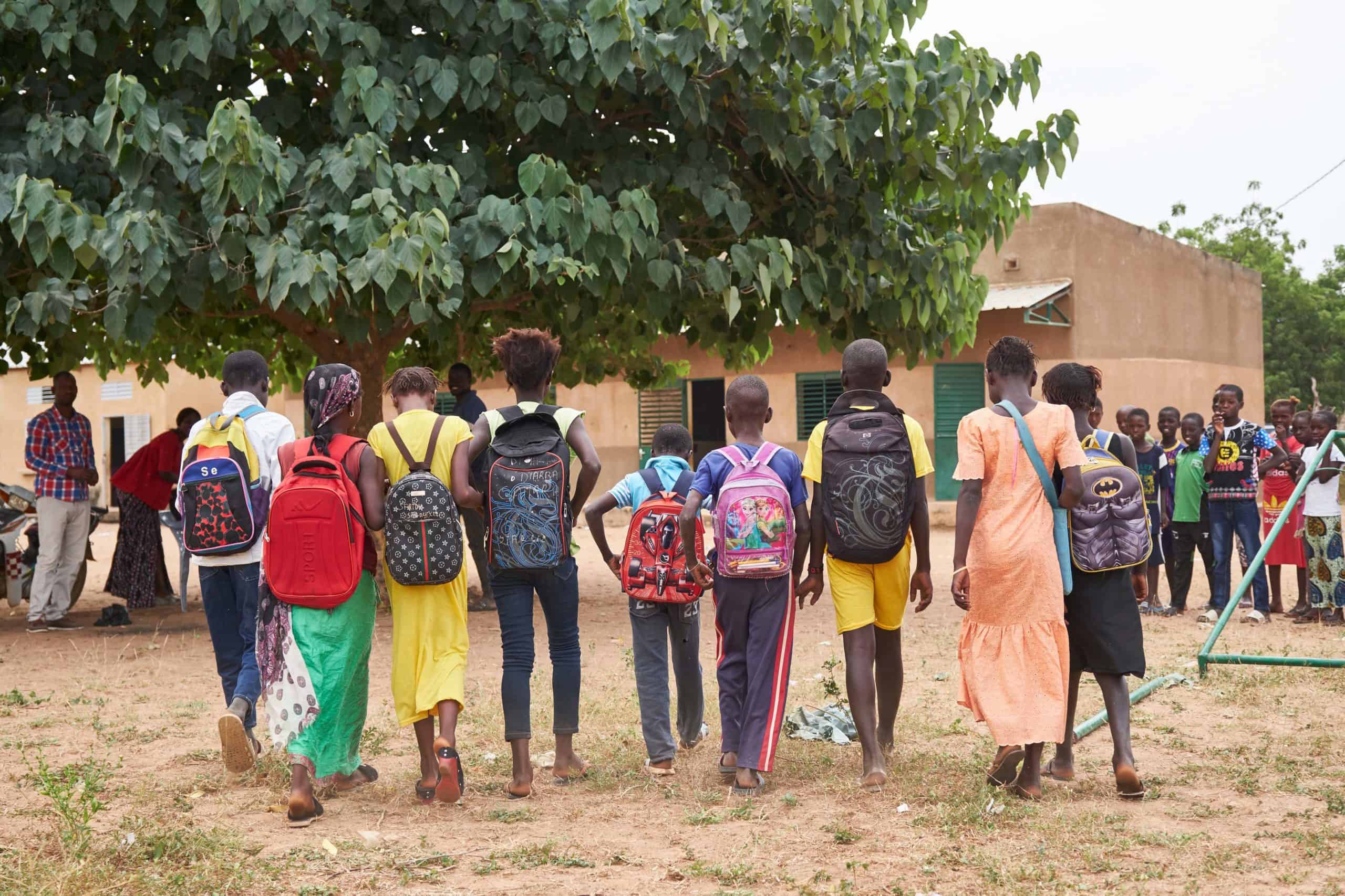 Group of children with backpacks walking towards a school building, part of a community initiative associated with Forest Garden projects