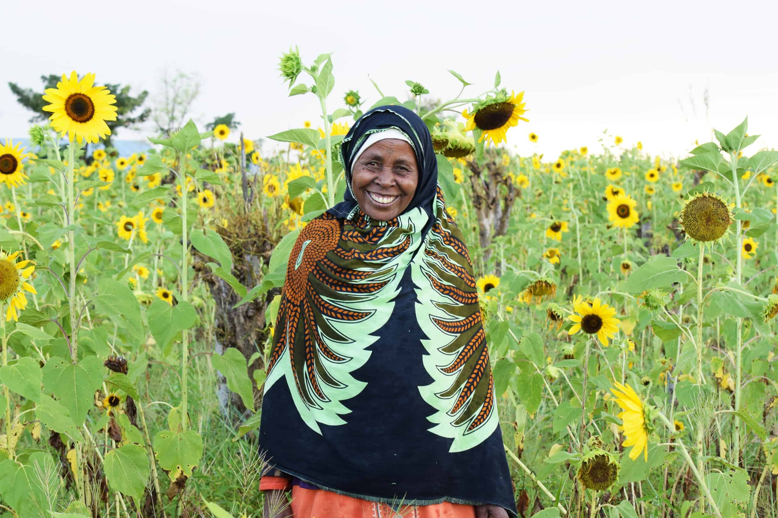 Smiling woman in vibrant attire standing in a sunflower field.