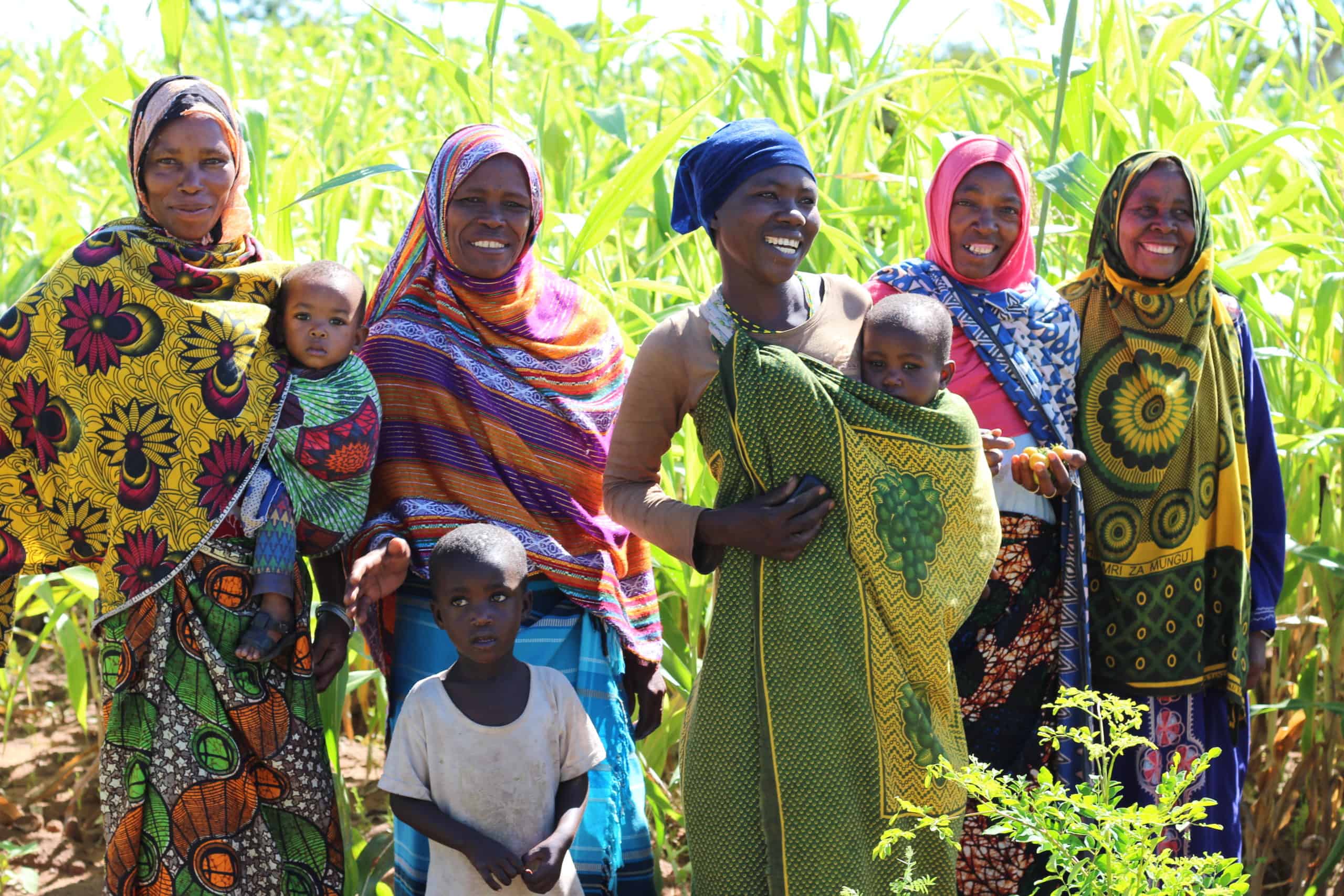 Group of smiling women and children standing in a vibrant field.